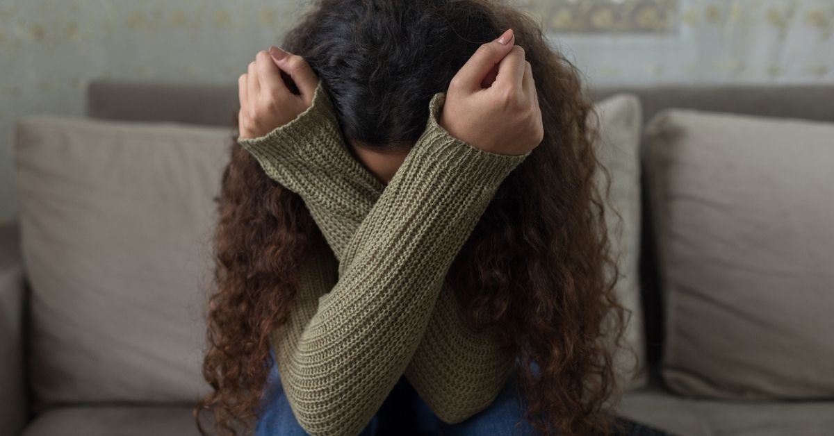Woman on couch covering her face with her arms
