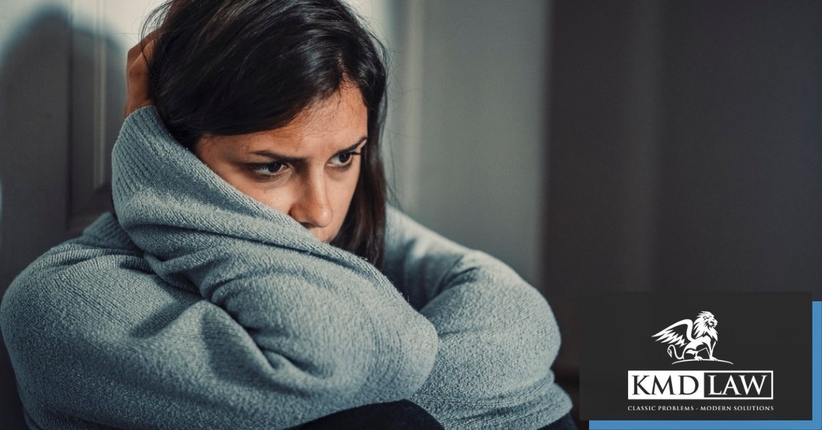 Woman sitting against a wall holding her head looking forward