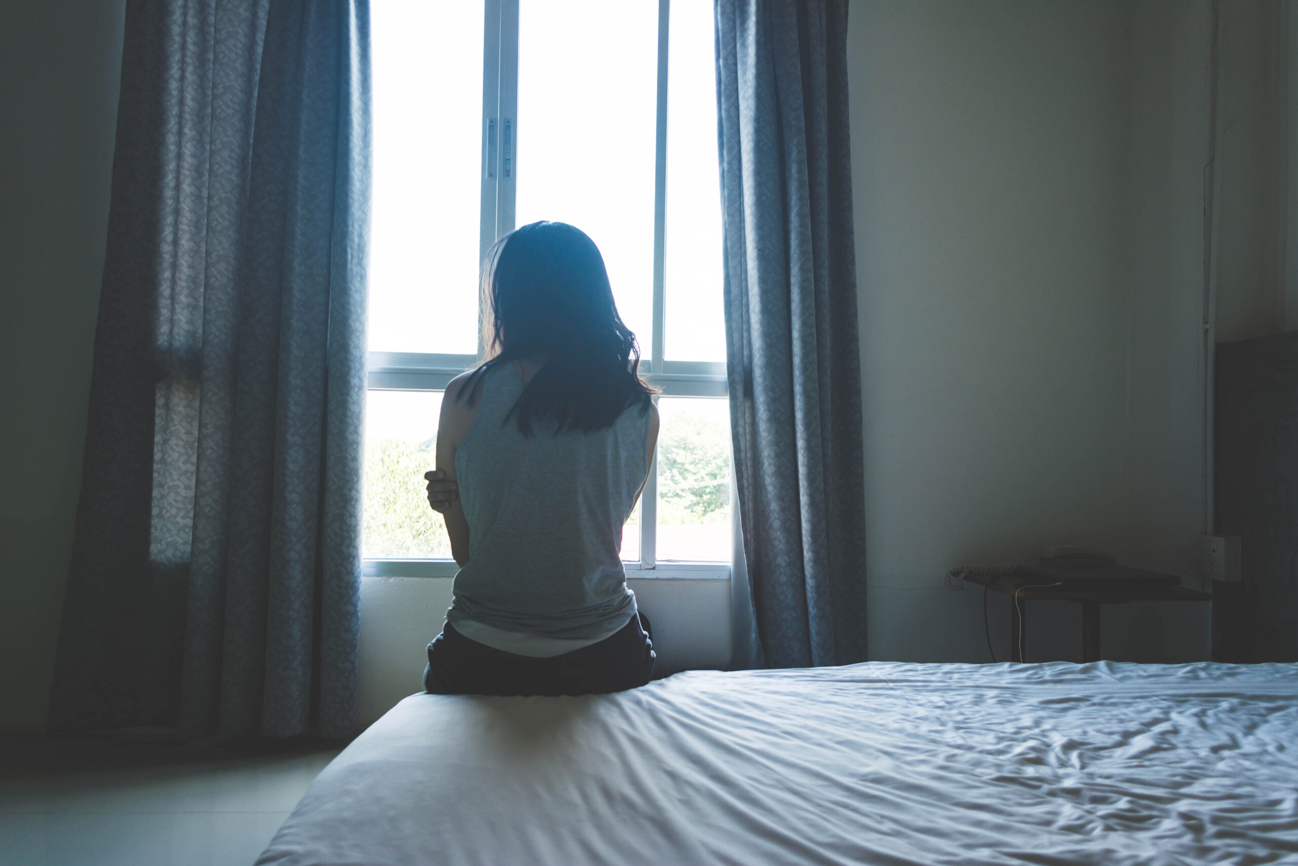 woman sitting on bed in room with light from window abuse concept