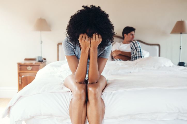Woman sitting on edge of bed with head in hands