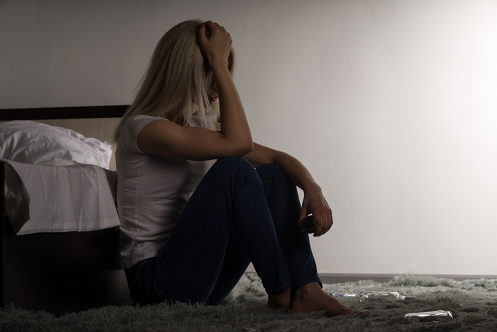 Woman sitting against bed and staring at floor