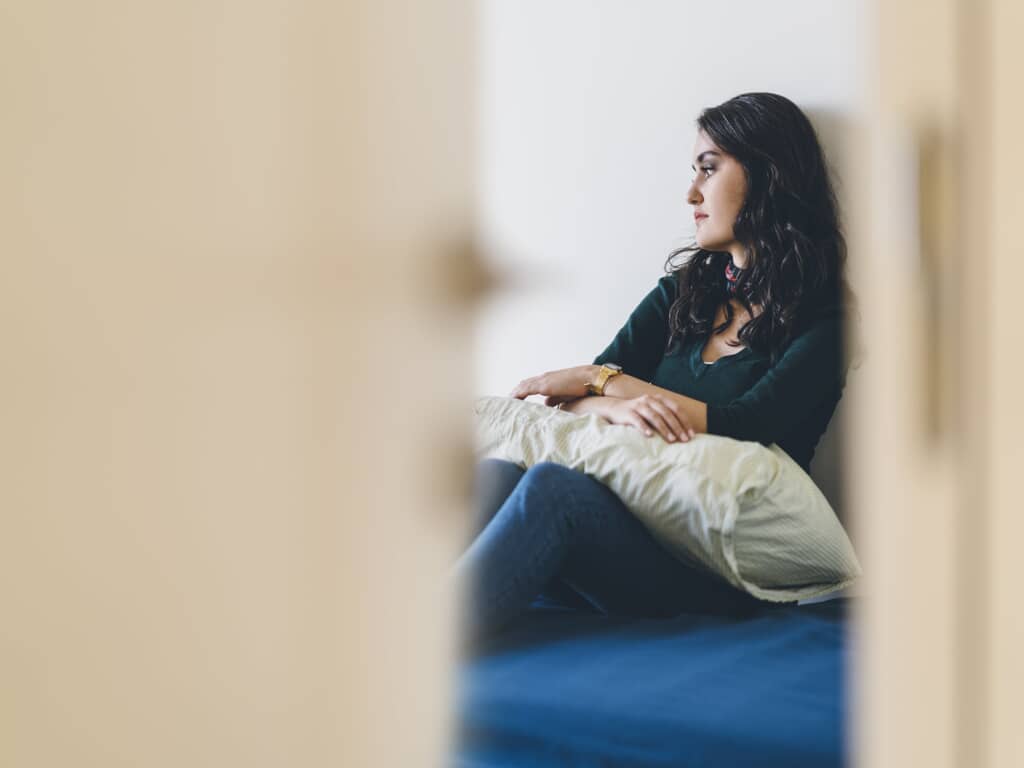 Woman sitting against wall with pillow on lap