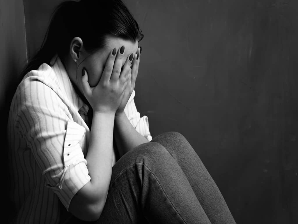 Woman sitting in corner with hands on face